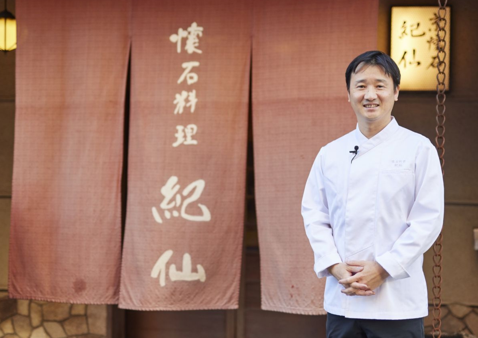 店舗の入口の暖簾前で料理人が写っている写真