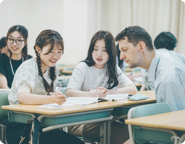 教室で外国人教師と一緒にテキストを見る学生たちの様子